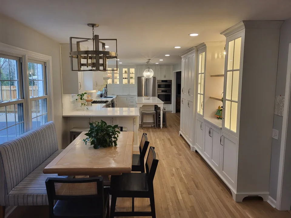 Breakfast nook with banquette seating beside a wall of tall built-in pantry cabinets and a lighted glass-front hutch.