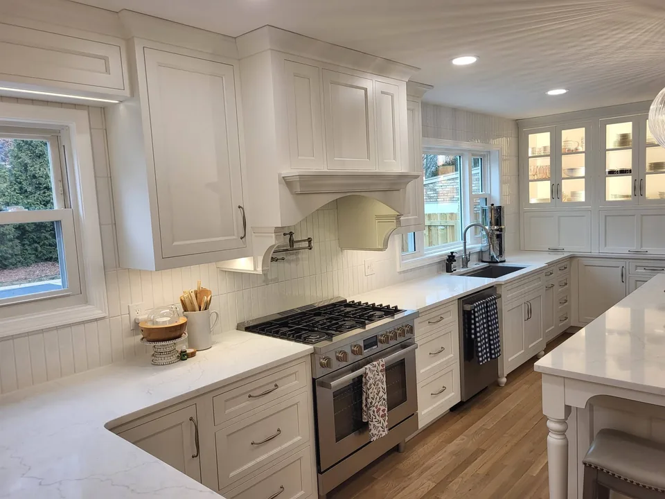 Custom white range hood with arched valance and corbels over a professional range, flanked by inset cabinetry and lighted glass display uppers.